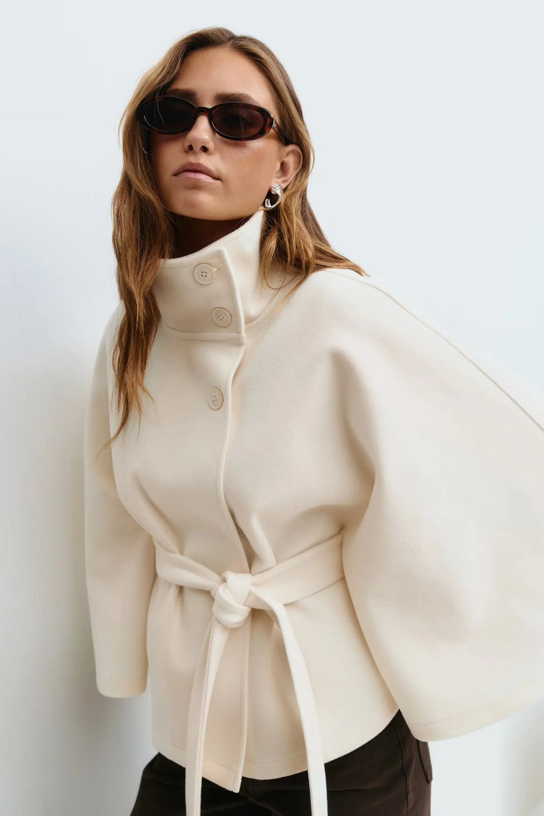 Beige Damen Cape-Mantel mit Stehkragen, Gürtelbindung und klassischem Design aus warmem, weichem Material.