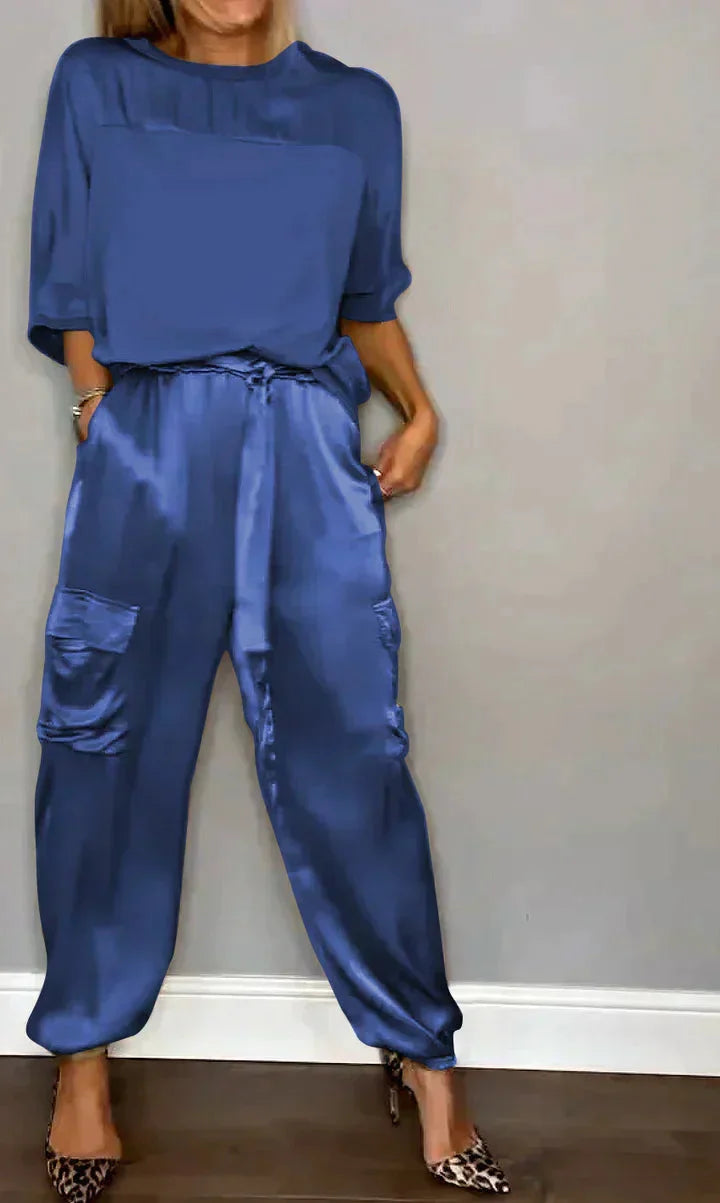 Blauer Damen Satin Jumpsuit mit Taschen, Bindegürtel und weitem Bein für einen lässigen, eleganten Look.
