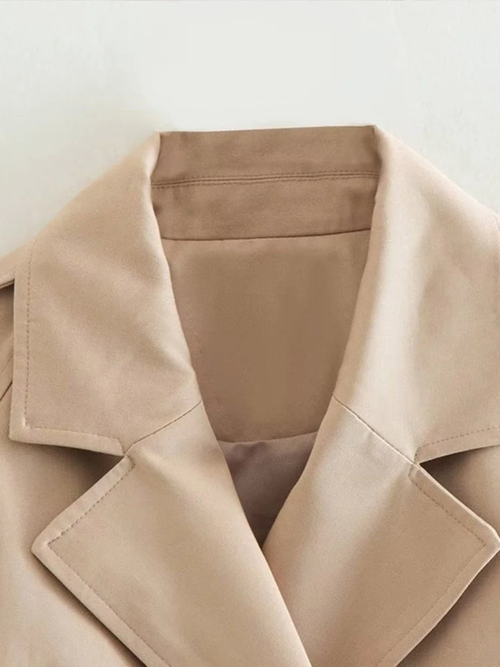 Beiger Damen Trenchcoat kurz mit Taillenbetonung, hergestellt aus leichtem Material mit modernen Knopfdetails.